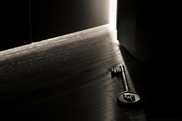 A metal key lying on the floor in front of a slightly open door