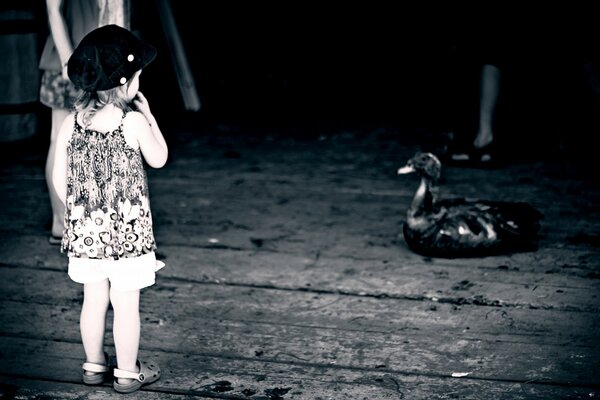 Una niña con ropa de verano frente a una mujer sobre un fondo blanco y negro observa a un gran pájaro negro