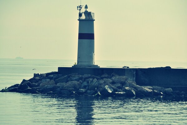 Lighthouse in the sea on a concrete pedestal surrounded by stones