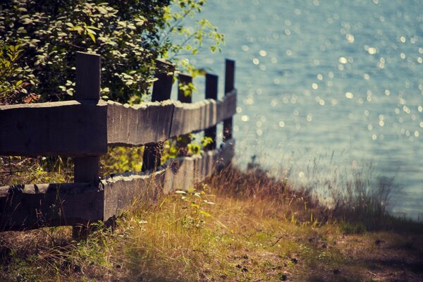 Holzzaun zwischen Gras und Wasser im Hintergrund