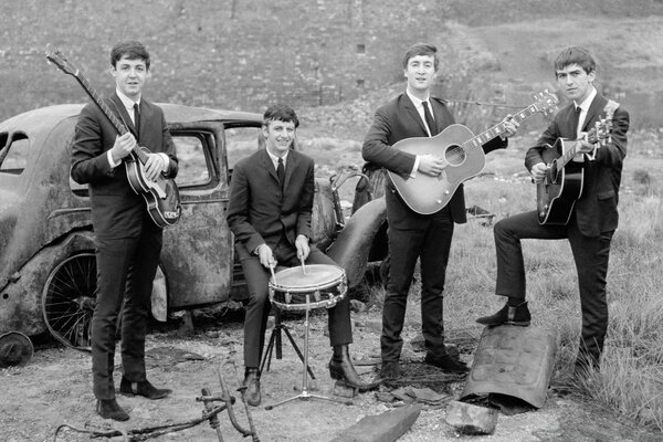 Zespół Beatlesów z instrumentami muzycznymi na tle zabytkowego rozpadającego się samochodu