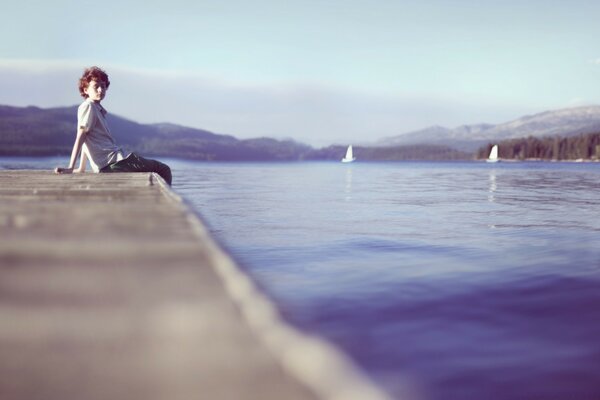 A lonely boy is sitting on the dock