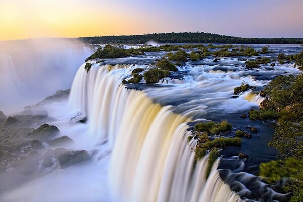 Falling waterfall and green forest at dawn