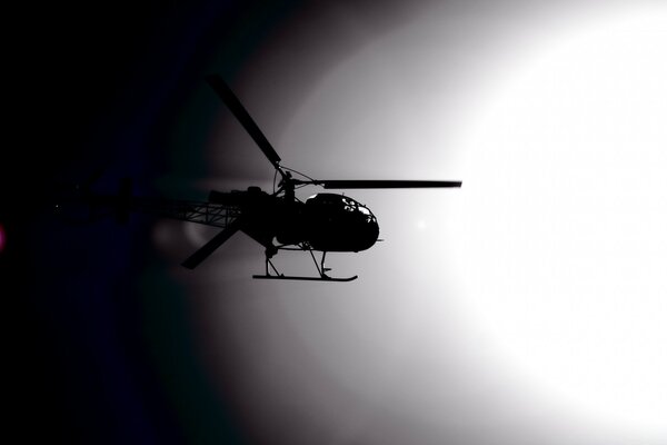 The silhouette of a helicopter under the white sun