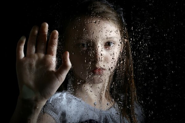 The girl looks through the wet glass