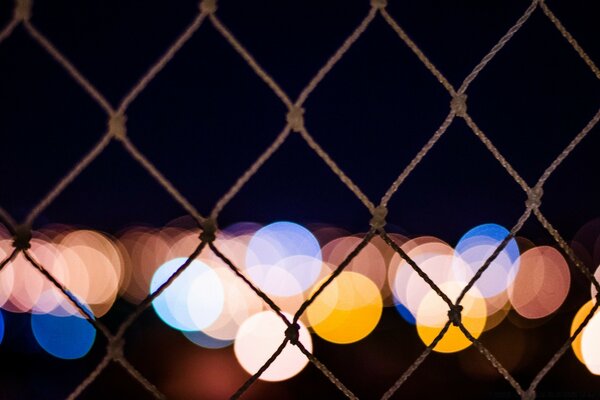 Hinter dem Gitter des Zauns auf schwarzem Hintergrund bunte Lichter