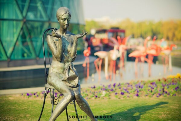 Estátua de uma menina sentada em uma cadeira no fundo de um flamingo