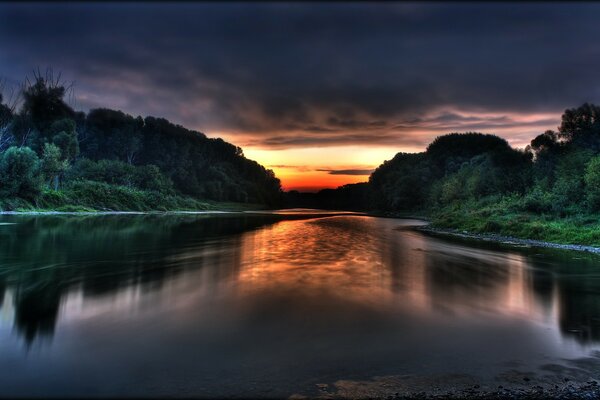 Rivière tranquille au coucher du soleil sous un ciel sombre