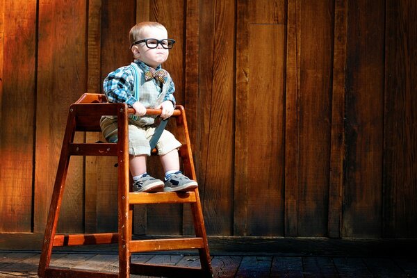 A child with glasses is sitting on a high wooden chair