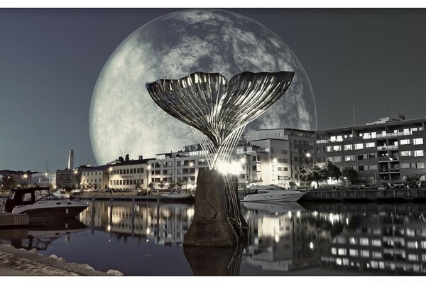 A monument in the form of the tail of a silver fish sticks out of the river against the background of the setting Moon and the night city