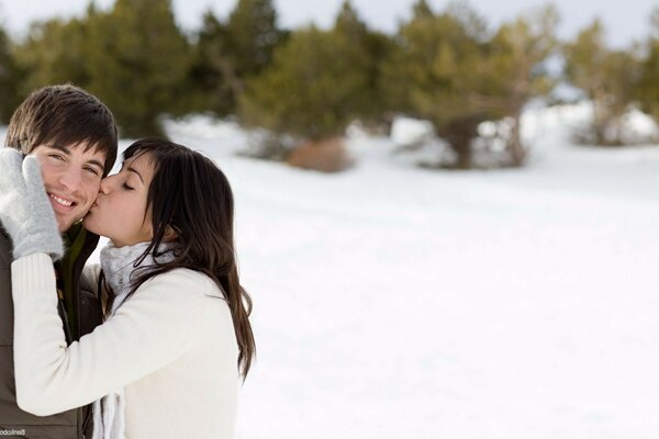 Chica besando a un chico en un claro de nieve