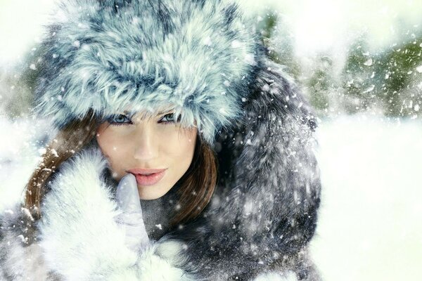 A girl in a fluffy hat is dusted with snow