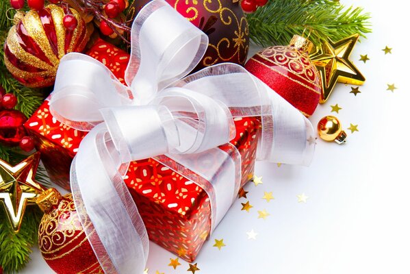 A red gift box with a white bow among Christmas toys and fir branches