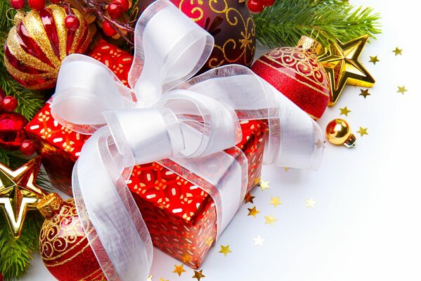 Caja de regalo de color rojo con lazo blanco entre juguetes de Navidad y ramas de abeto