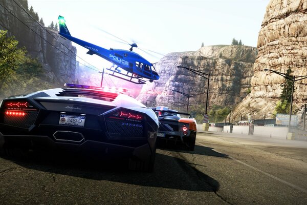 Two sports cars are driving along the road passing between the rocks, a helicopter is hovering over them