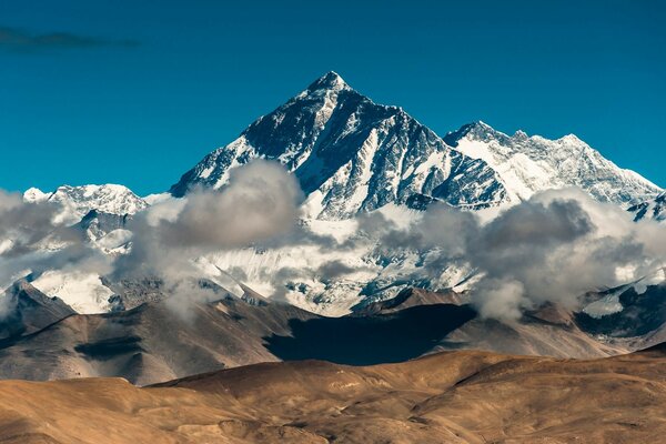 बादलों के ऊपर एक बर्फ से ढकी पहाड़ी की ऊंचाई