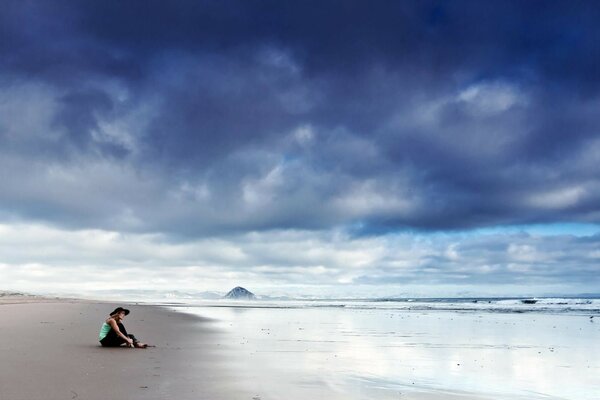 Chica sentada en la orilla del mar en el cielo nubes oscuras