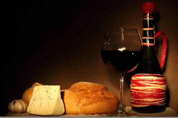 Jug, glass with red wine, cheese with mold, bread, garlic