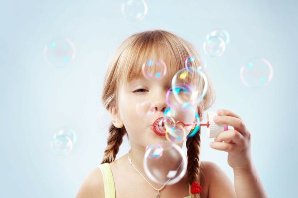 A little girl with pigtails inflates soap bubbles