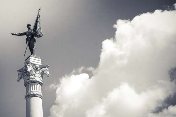 Sculpture on a pedestal with a flag against the sky