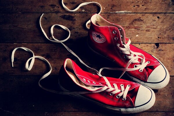 A pair of red Converse sneakers on a wooden floor with loose laces