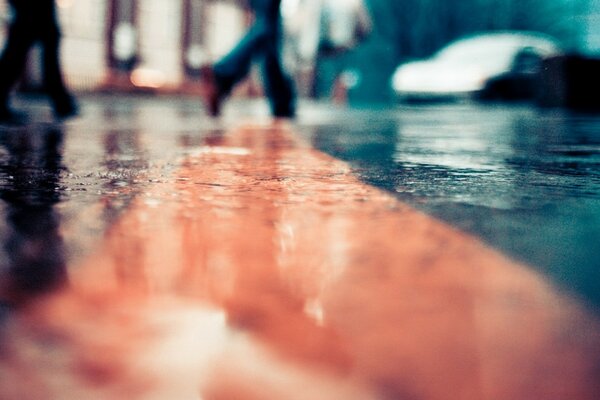 Macro of an asphalt road, wet from the rain, along which people are walking