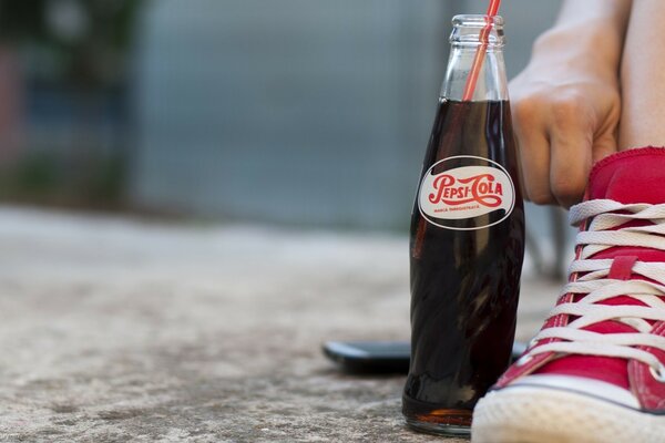 Jemand sitzt entspannt in Turnschuhen mit einer Flasche Pepsi-Cola auf Beton