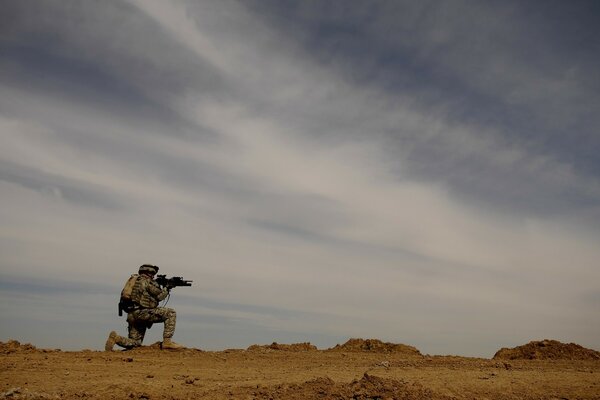 A soldier takes aim at someone in the desert