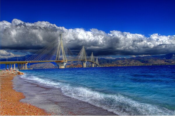 Die Brücke über dem Meer geht in die Wolken. Blauer Himmel. Gelber Sand