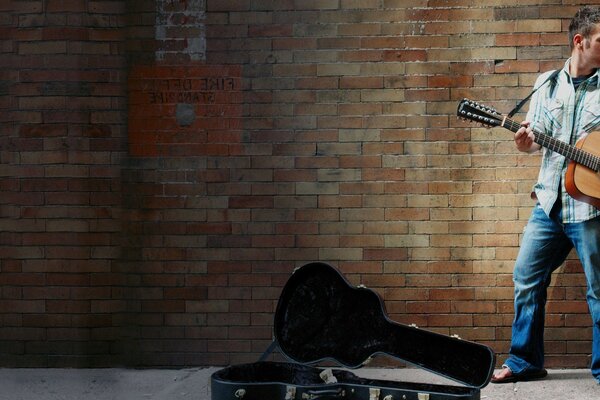 A street musician plays guitar for passers-by, standing against a brick wall