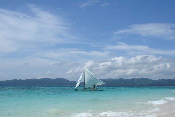 A lonely sailing boat on the water surface of a tropical sea against a cloudy sky