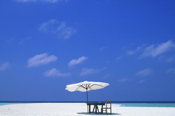 Tisch unter einer Markise am Strand des azurblauen Meeres