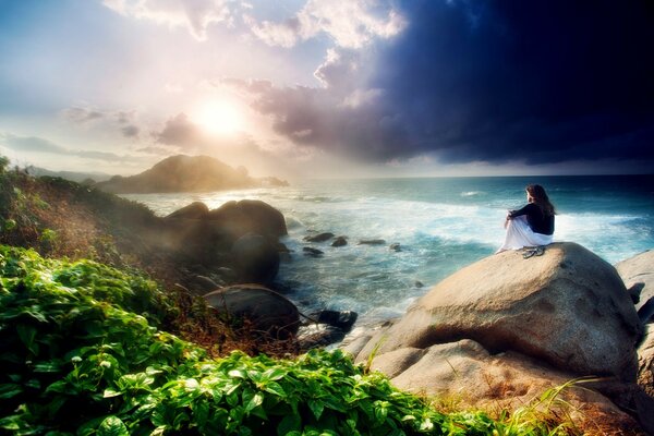 A girl sitting on a rock on the seashore