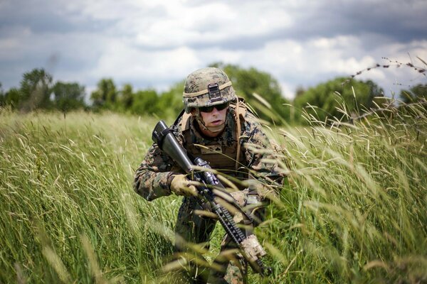 Солдат в униформе пробирается сквозь высокую траву в поле