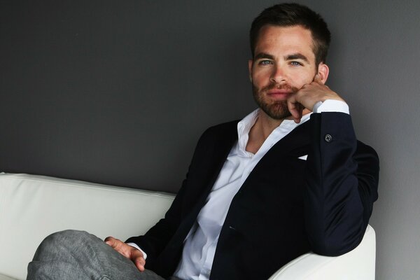 A handsome actor in a suit is sitting on the couch