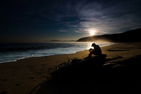 The traveler by the sea is illuminated by the dim rays of the sun behind the mountain