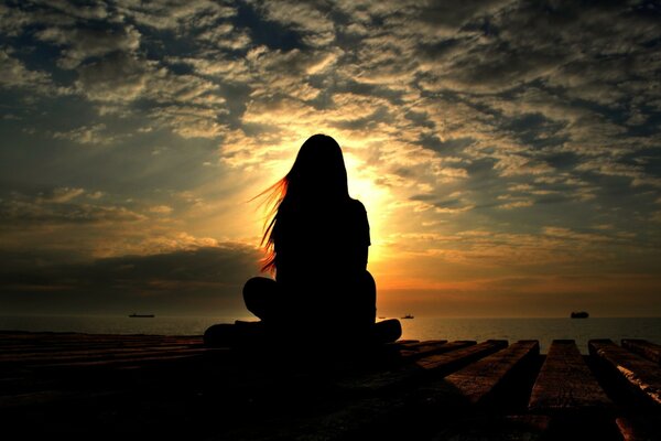 Silhouette eines Mädchens, das in einer Lotus-Pose sitzt, schloss die Sonne