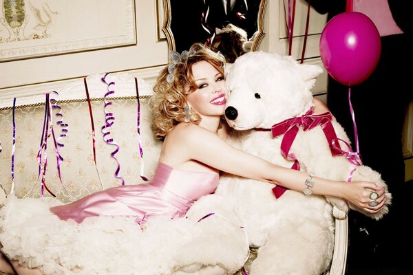 Deushka in a pink dress hugs a white teddy bear