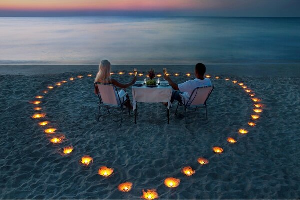 Zwei Liebende bei einem romantischen Abendessen unter Kerzen am Meer