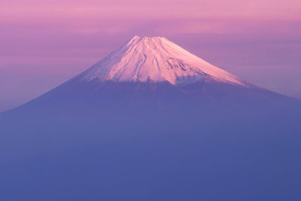 A snow-covered volcano in a pink-purple fog