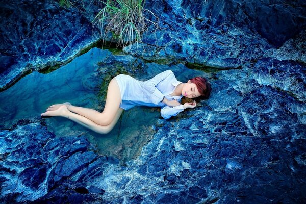 Una ragazza con una camicia bianca giace su un fianco in acqua. Paesaggio in colori blu