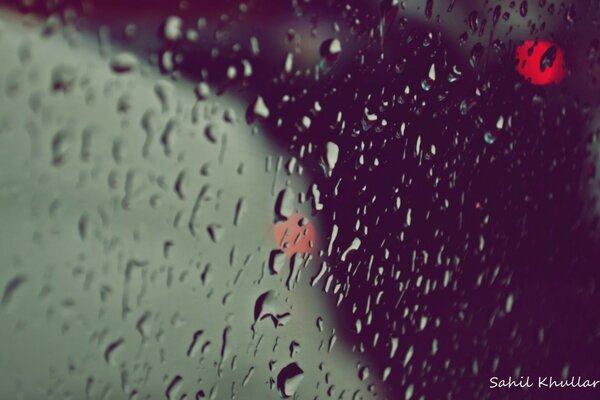 Image of water droplets on glass with red lights