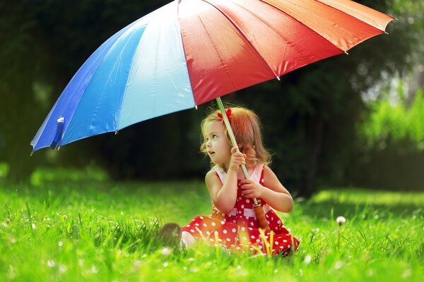 Mädchen in einem Polka Dot-Kleid, das unter einem riesigen hellen Regenschirm auf dem Rasen sitzt