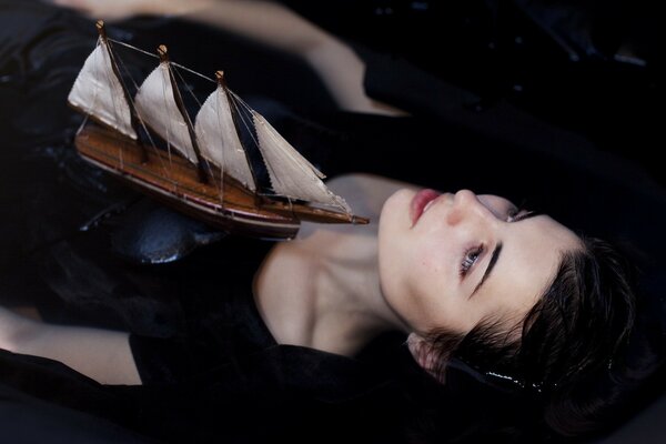 A model sailboat floating over a girl lying in the water