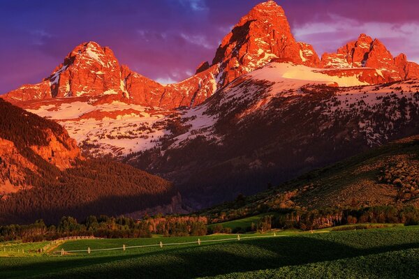 Montañas cubiertas de nieve con un Prado verde al atardecer