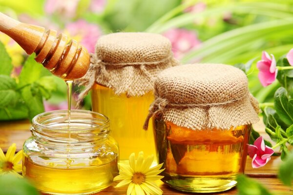 Three jars of honey surrounded by flowers