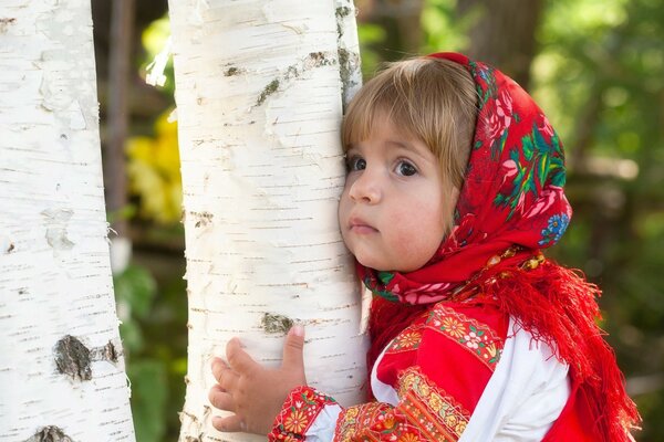 A girl in a red scarf hugging a birch tree