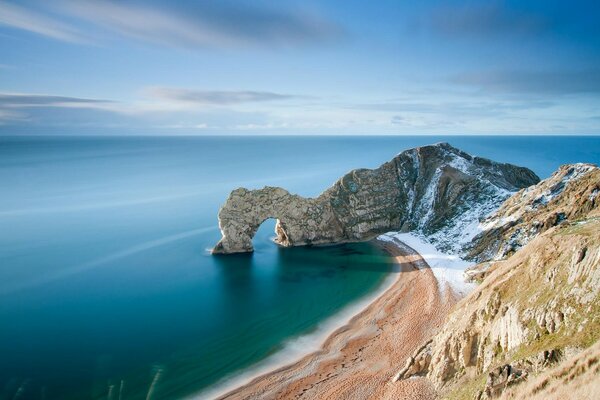 Sandy beach with blue sea and snow-covered rocks