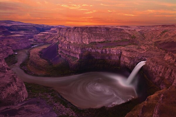 Pôr do sol em um canyon com uma cachoeira e um rio