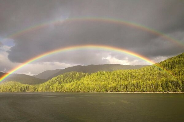 Doppelter Regenbogen über dem Fluss. Grüne Ufer